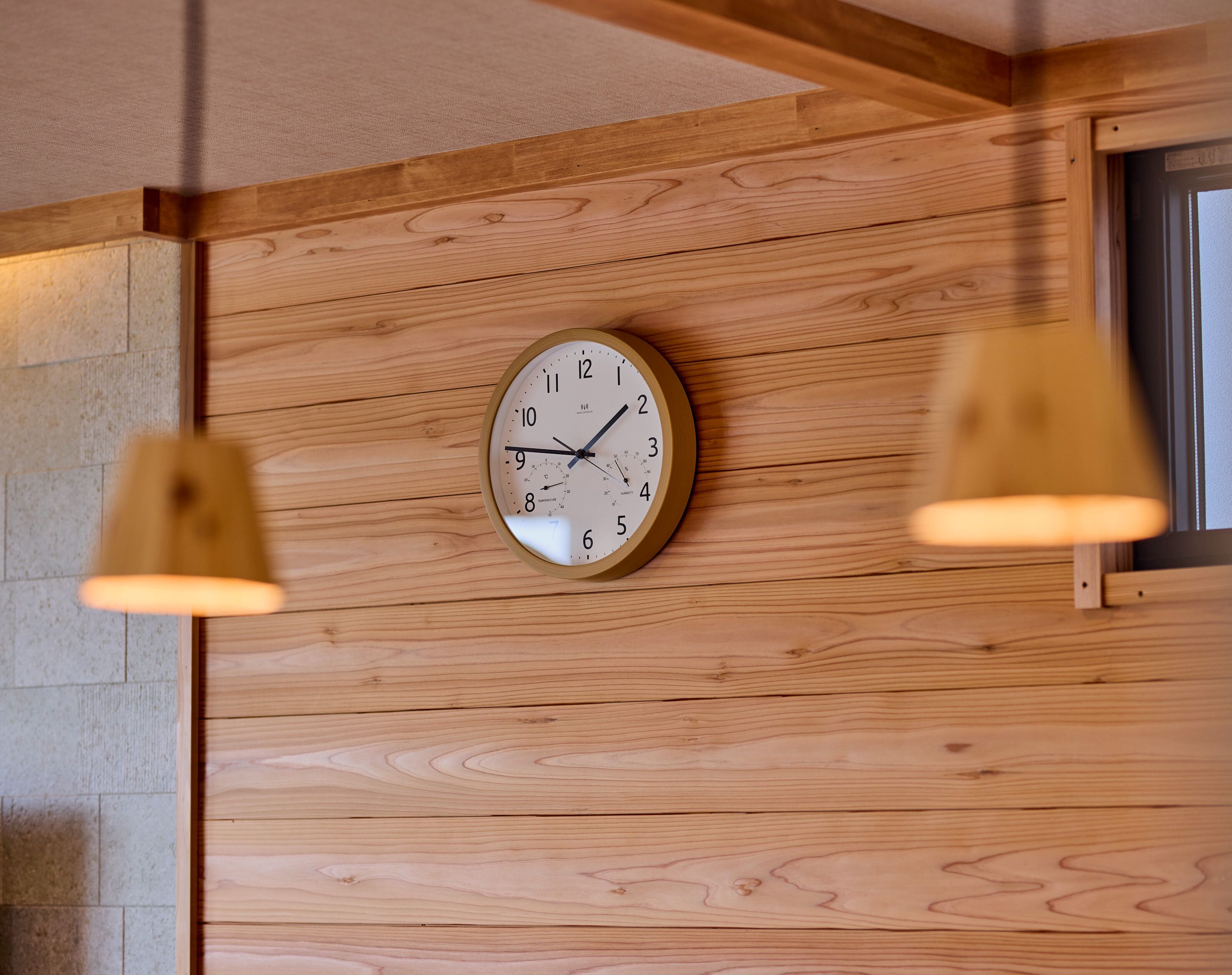 A wooden wall with a round wall clock and two pendant lights.