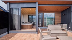 A modern outdoor patio with a hot tub, seating area, and sliding glass doors leading to a room. - Miire Mt.Fuji Forest (Fujikawaguchiko)