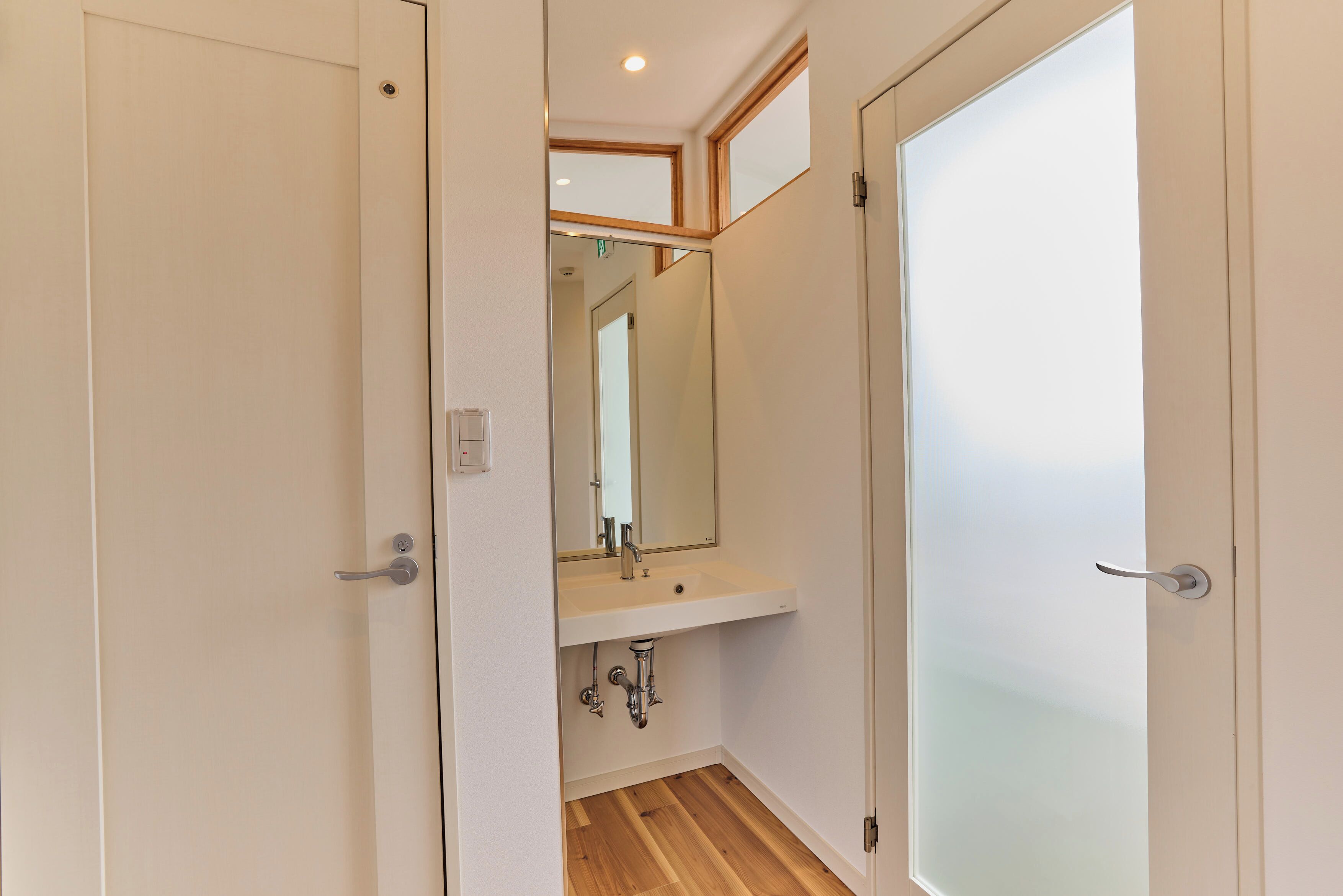 A narrow hallway with a white door on the right, a white wall, and a wooden floor.