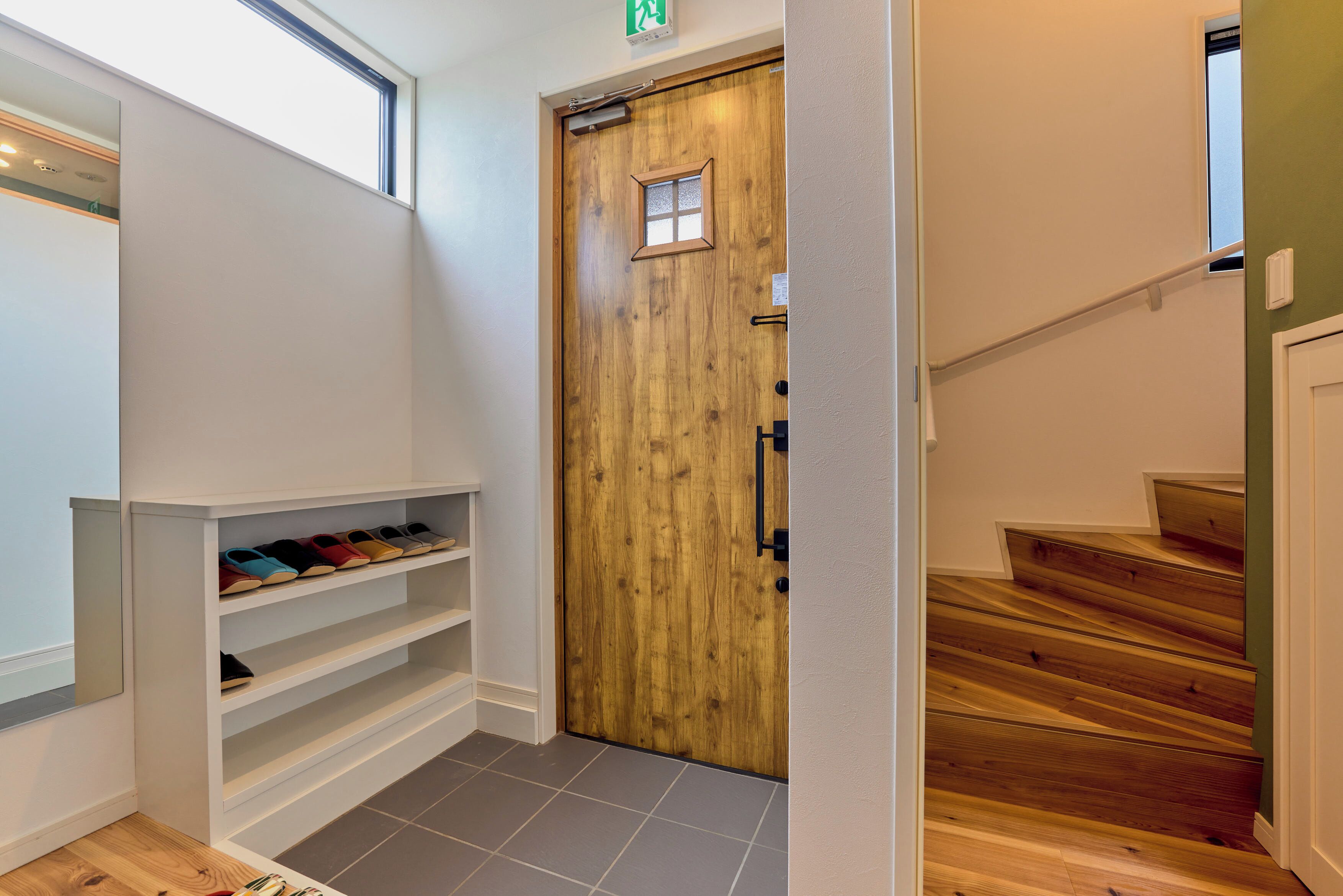 Une porte en bois avec une petite fenêtre, un porte-chaussures contenant plusieurs paires de chaussures et un escalier avec des marches en bois.