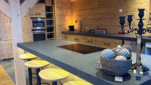 Een moderne keuken met houten balken, een centraal eiland met krukken, inbouwapparatuur en een decoratieve kandelaar.