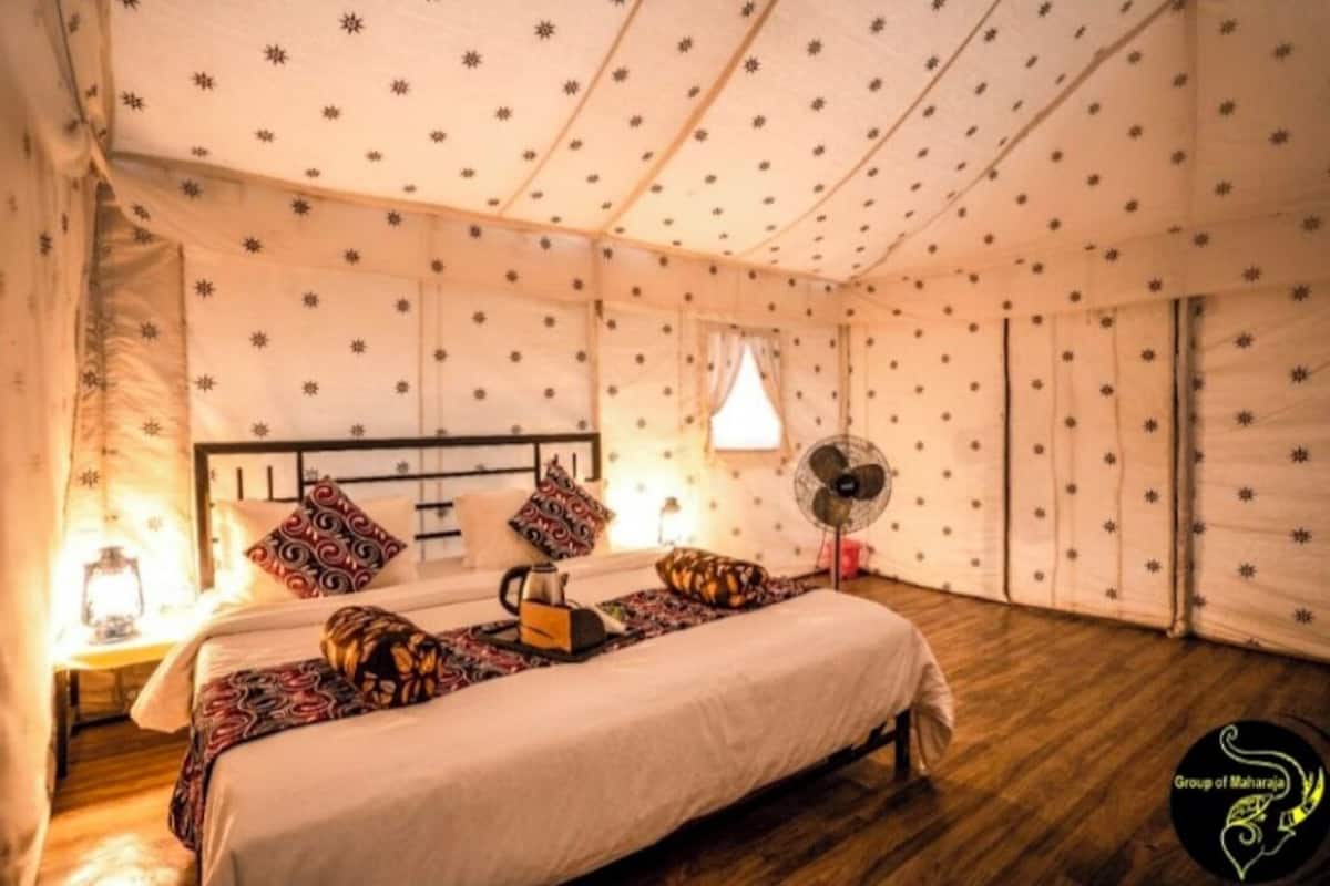 A cozy room with a bed, pillows, a bedside table with a lamp, and a fan.
