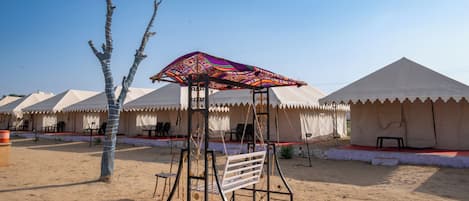 A desert setting with tents and a swing set.
