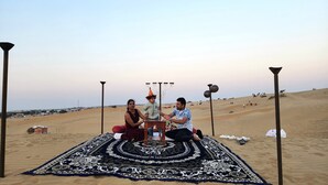 A desert scene with a group of people sitting on a patterned carpet. - Star Desert Camp Jaisalmer  (Jaisalmer)