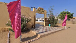 A desert camp entrance with a sign, a checkered pathway, and two pink flags. - Star Desert Camp Jaisalmer  (Jaisalmer)