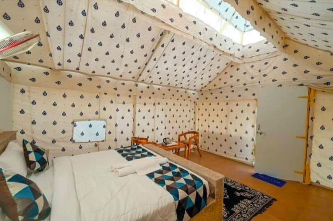 Une pièce aménagée comme une tente, avec un lit, une chaise, une petite table et une fenêtre.