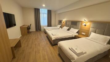 A hotel room with three beds, a desk, and a TV.
