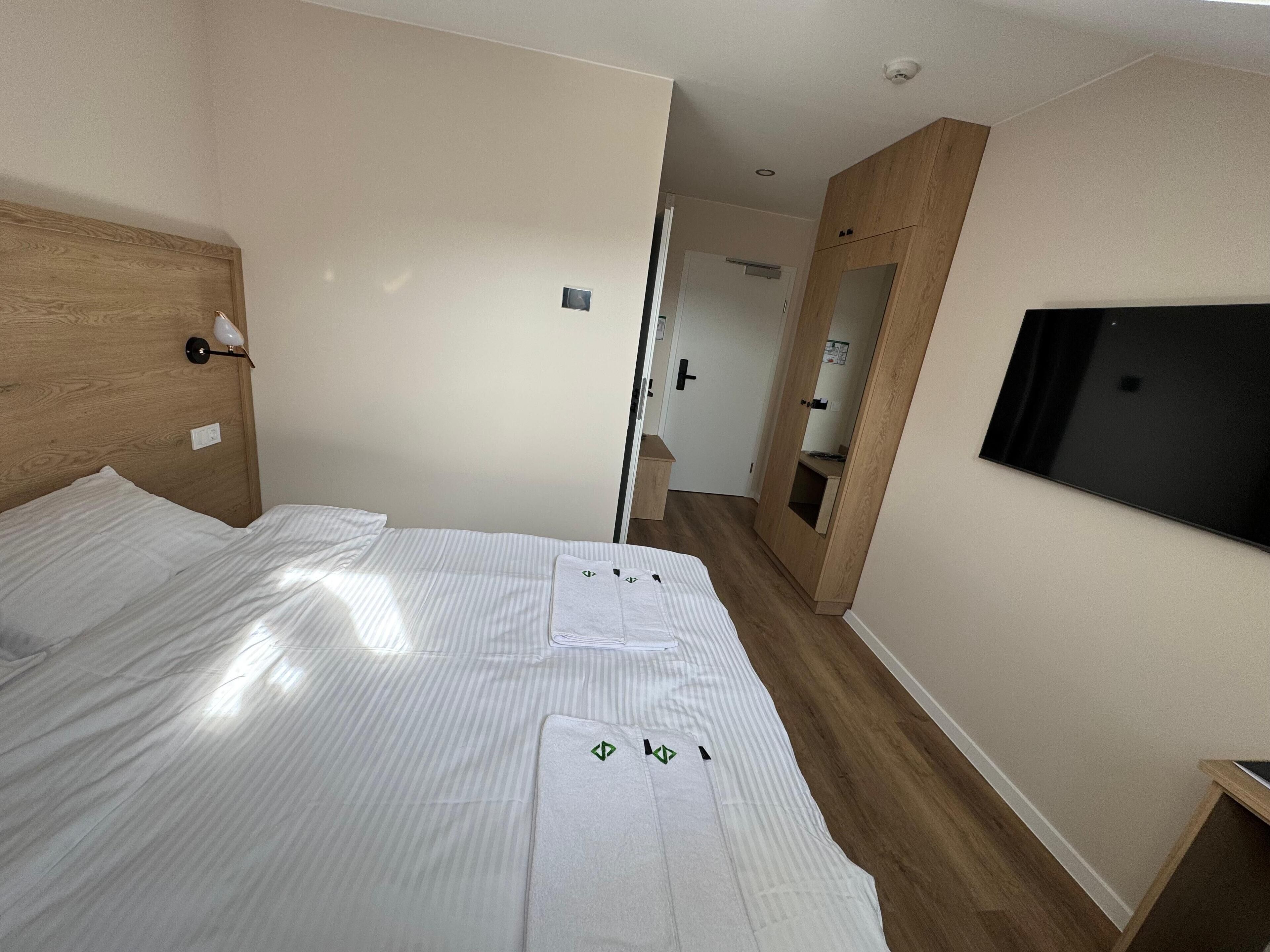 A hotel room with a bed, a TV, and a wooden wardrobe.