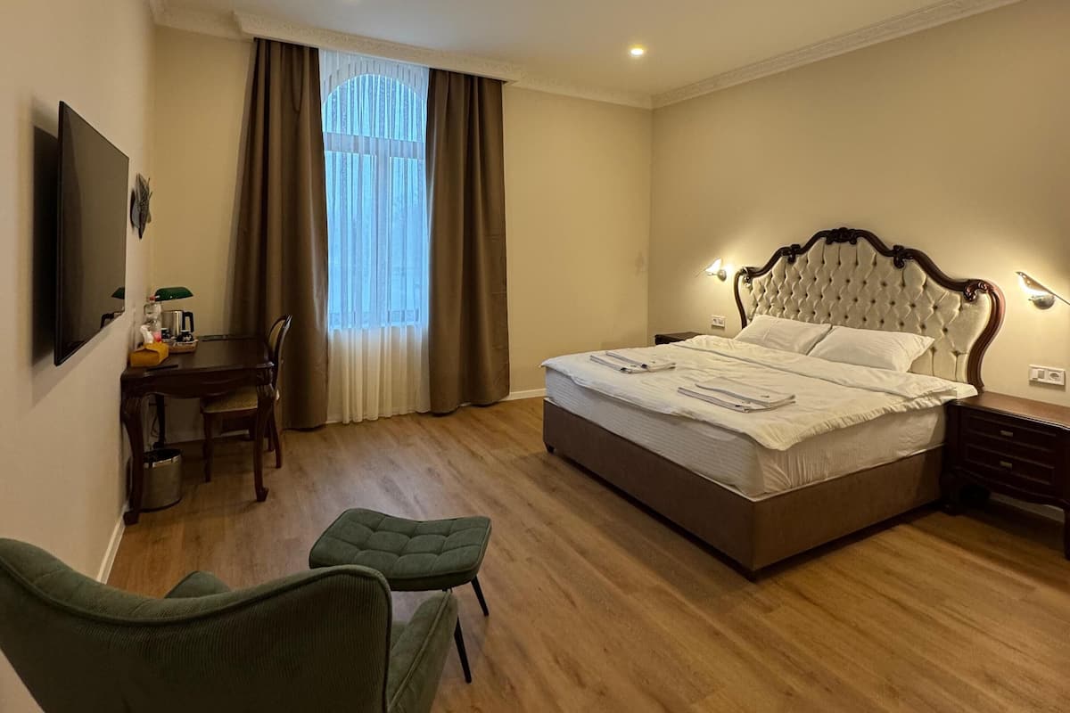 A bedroom with a large bed, a desk with a chair, a television, and a window with curtains.
