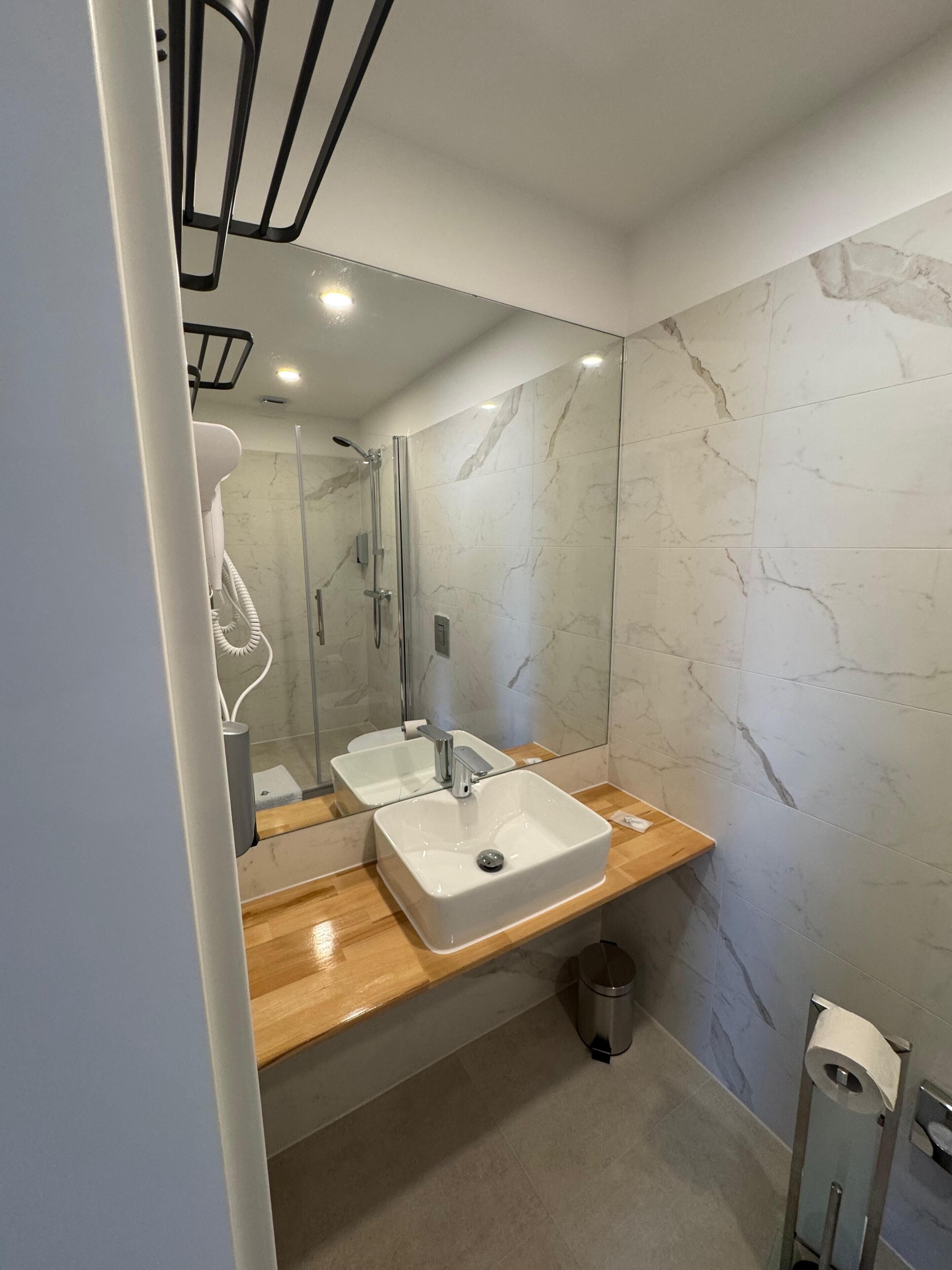 A modern bathroom with a large mirror, two sinks, and a shower.