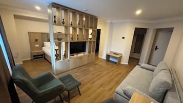 A living room with a sofa, two armchairs, a TV, and a wooden entertainment unit with shelves.