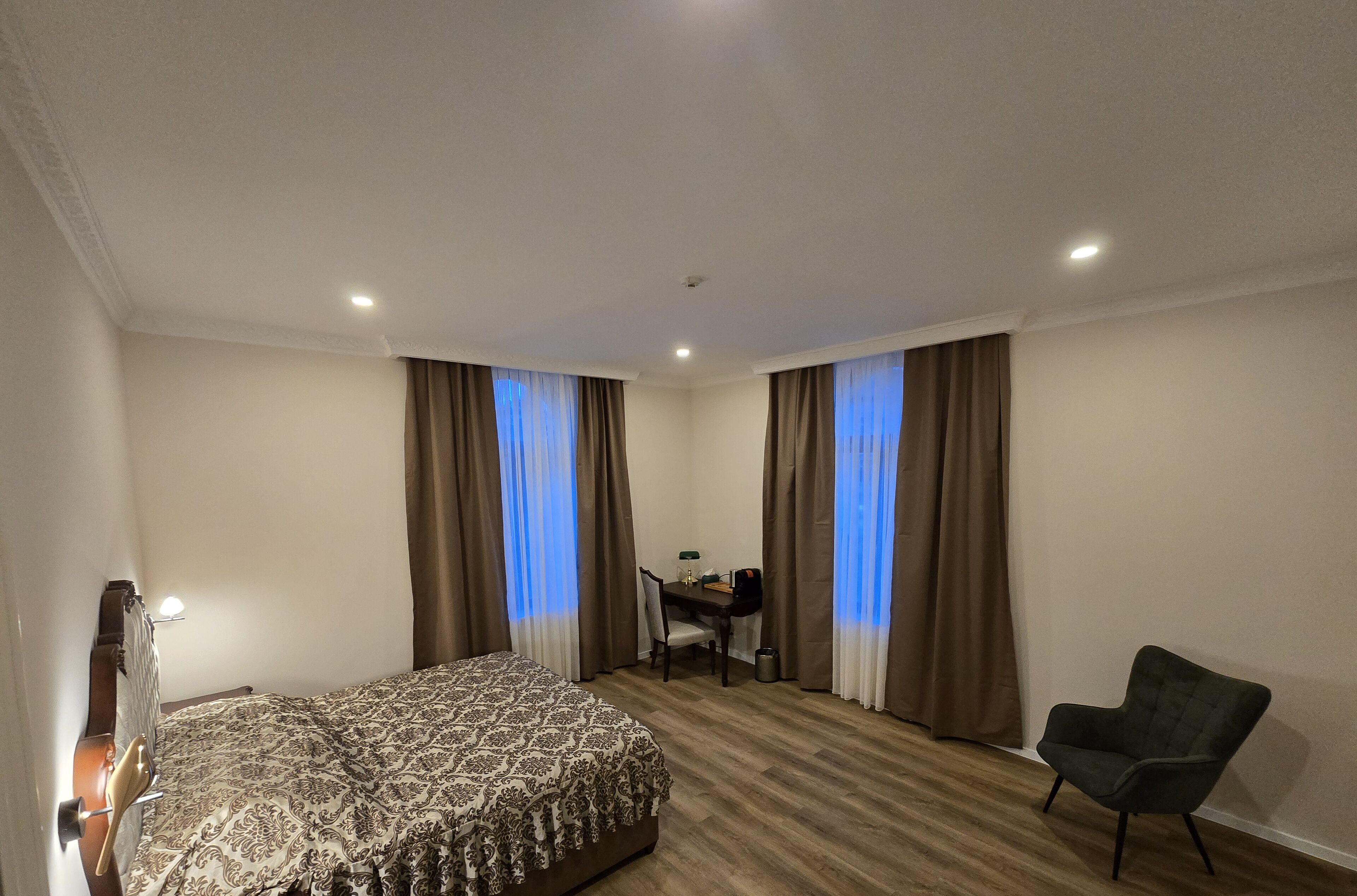 Una habitación de hotel con cama, escritorio, silla y ventana con cortinas.