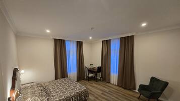 Una habitación de hotel con cama, escritorio, silla y ventana con cortinas.