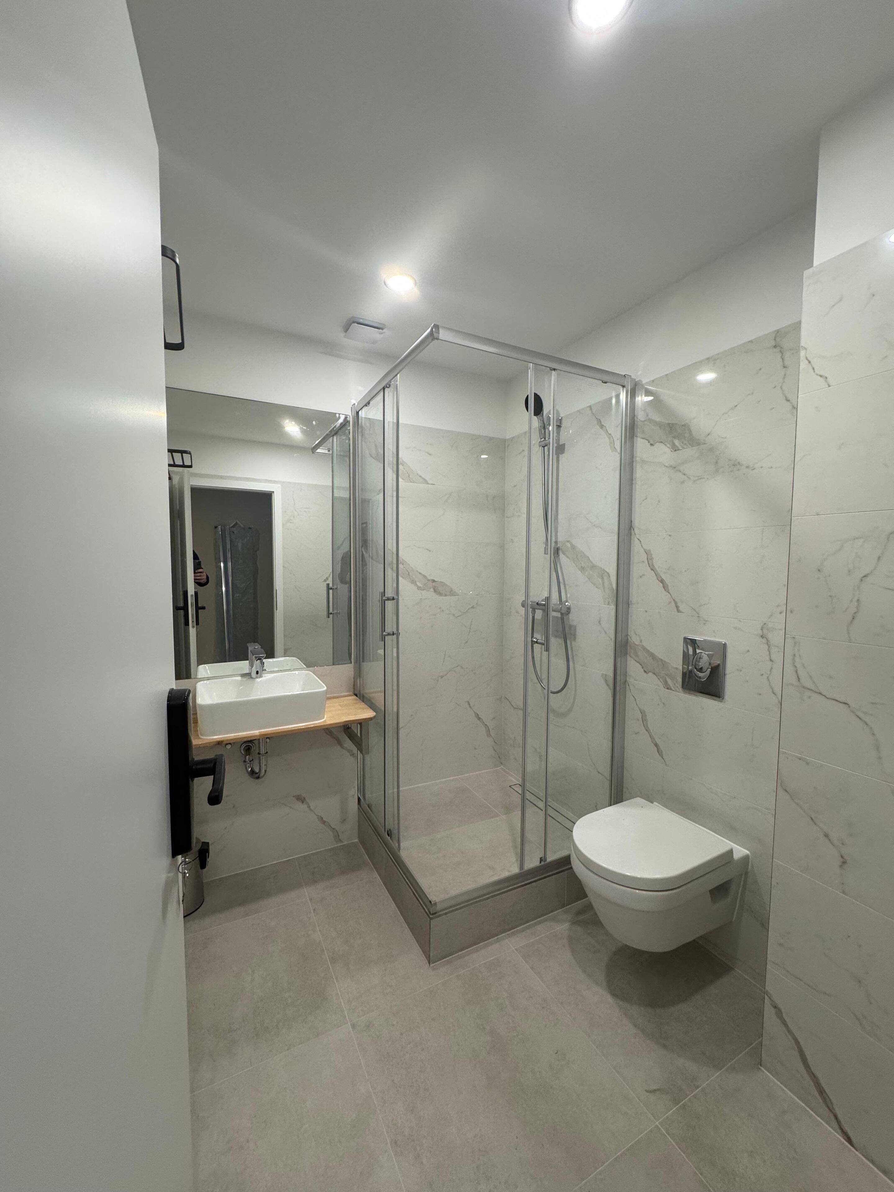 Ein modernes Badezimmer mit einer gläsernen Duschkabine, einem weißen Waschbecken und einer Toilette.