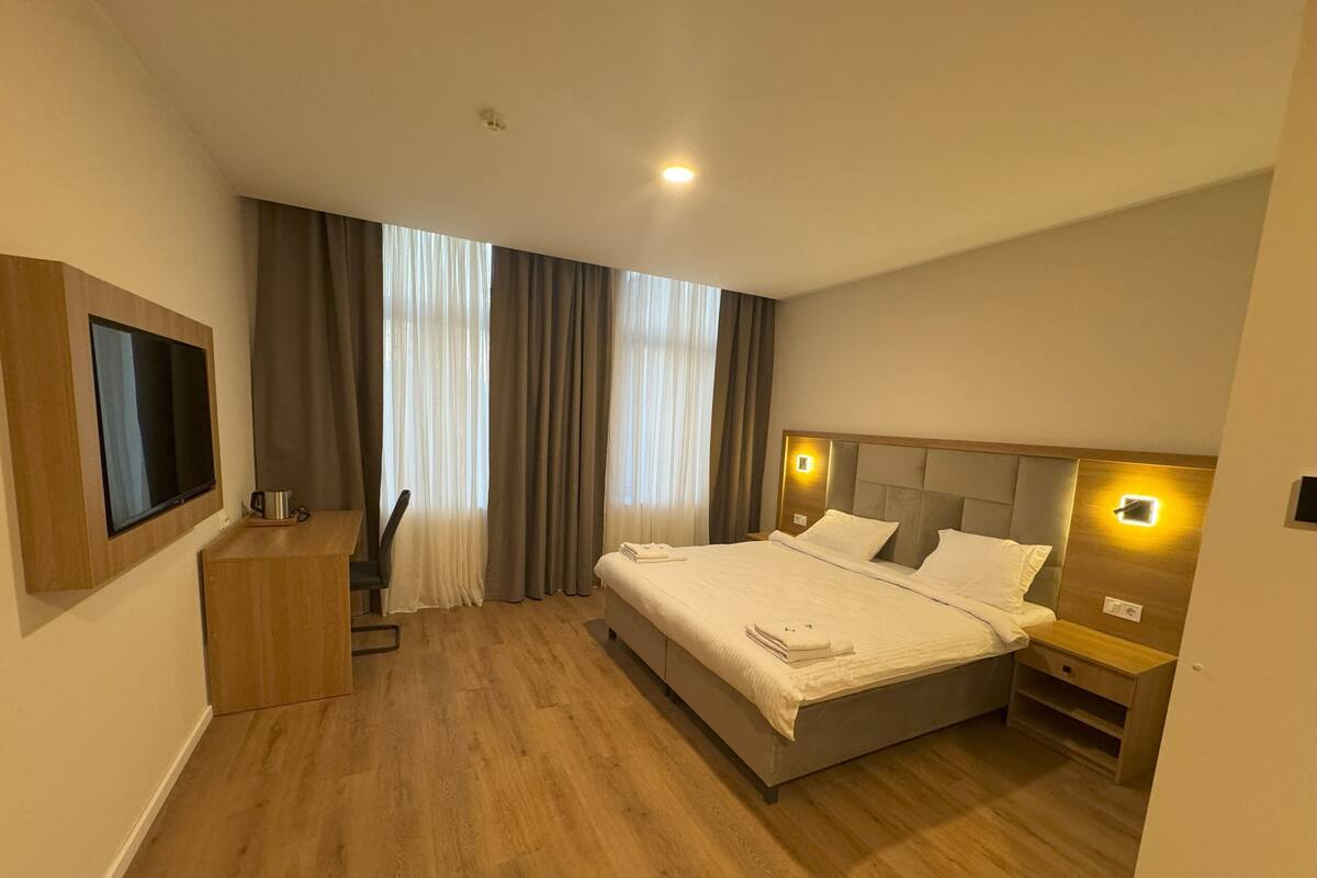A modern hotel room with a large bed, a flat-screen TV, a desk, and a chair.