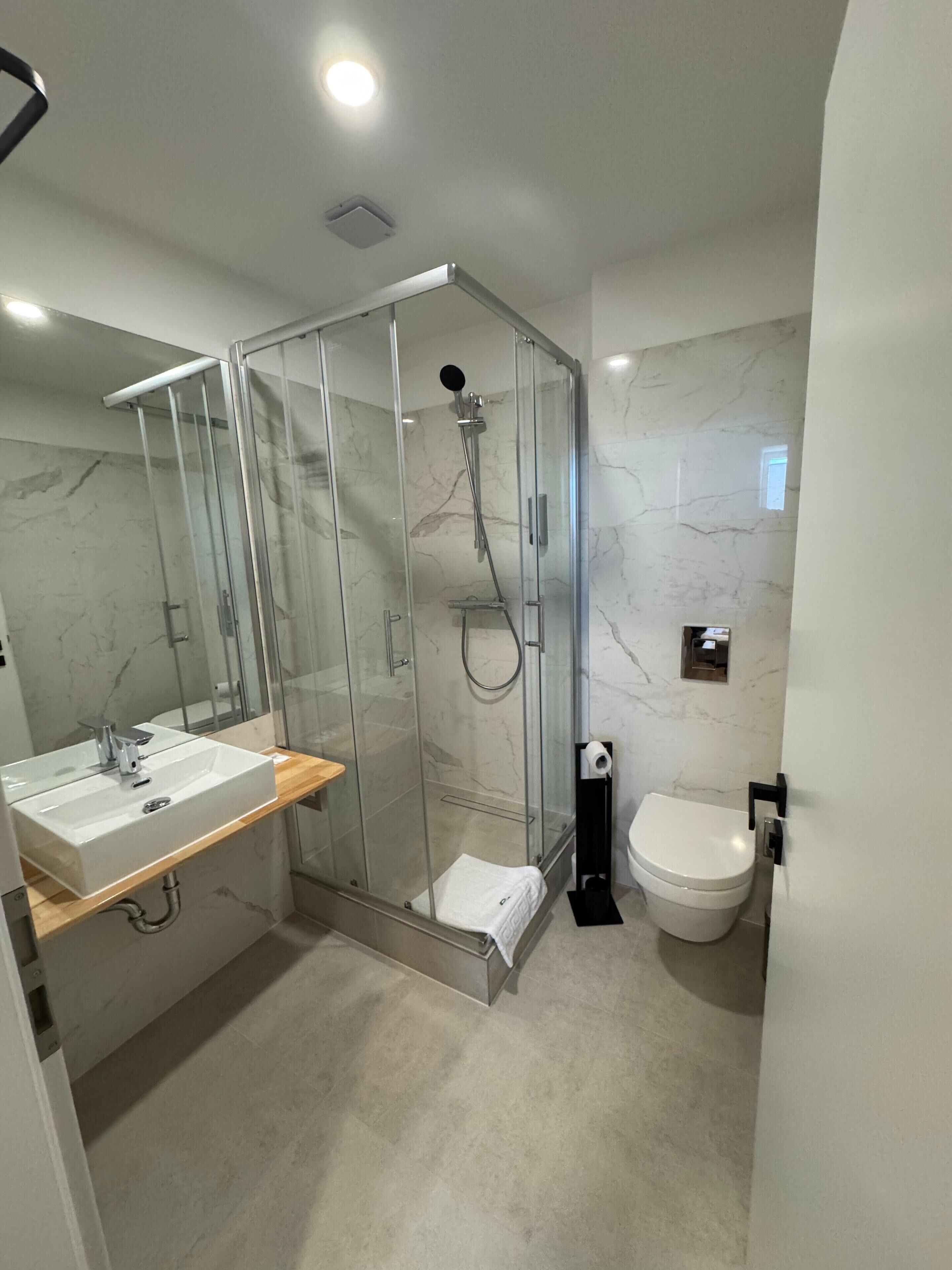 A modern bathroom with a glass-enclosed shower, a white sink with a wooden countertop, and a toilet.