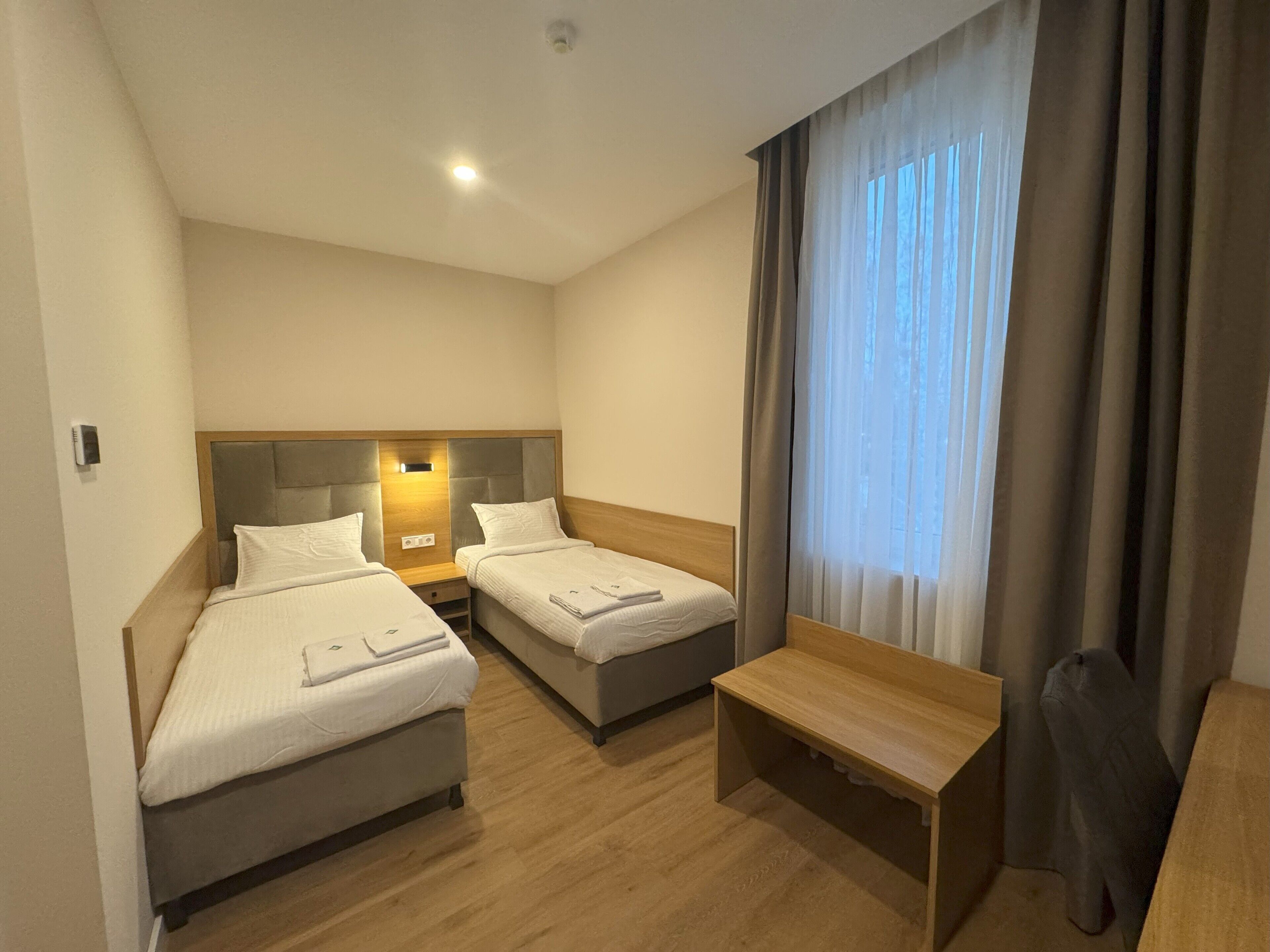 Habitación de hotel con dos camas, un escritorio y una ventana con cortinas.