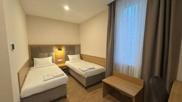 Habitación de hotel con dos camas, un escritorio y una ventana con cortinas.