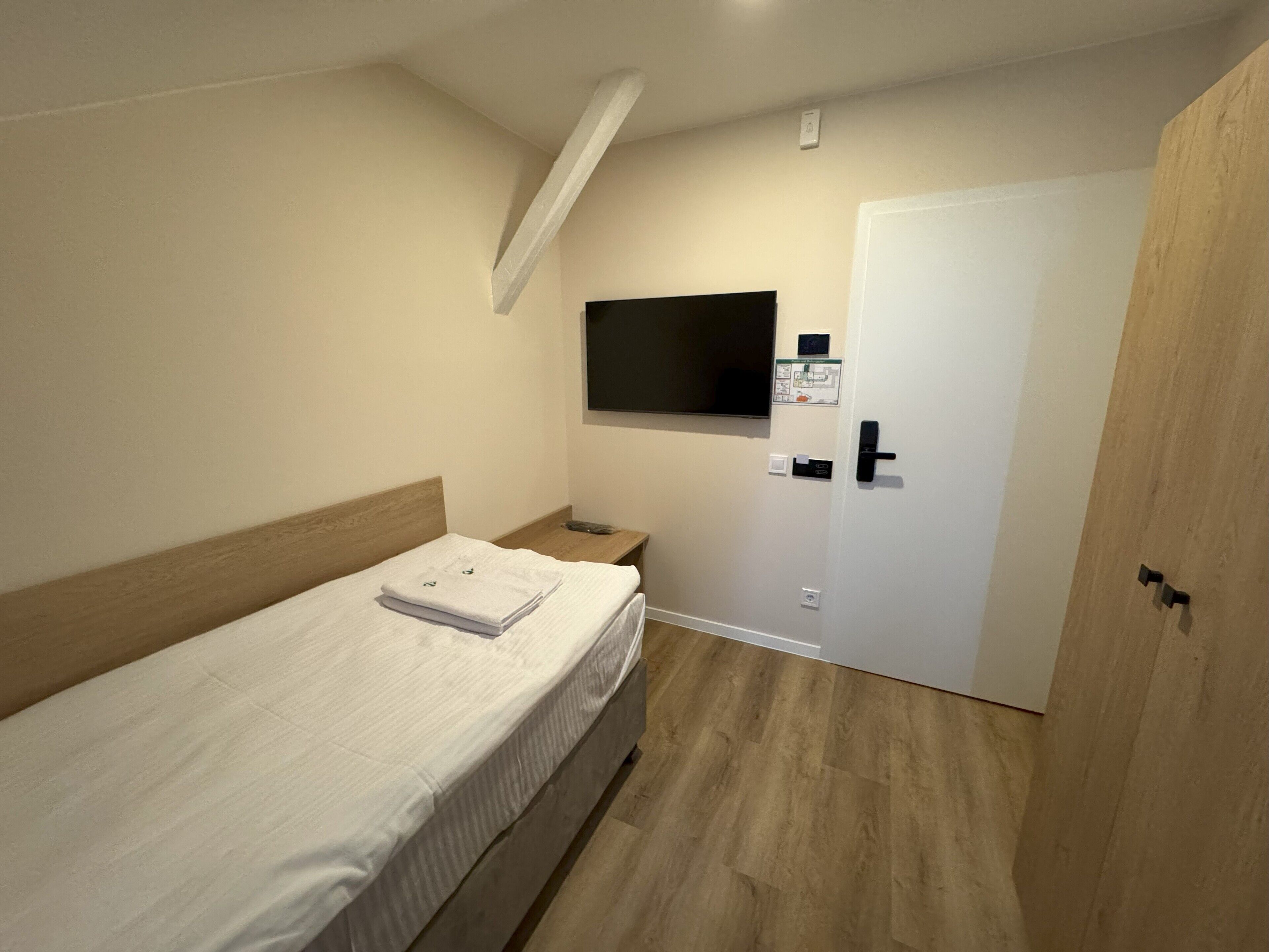 Une chambre d’hôtel avec un lit, un téléviseur fixé au mur, une porte en bois et une petite table.