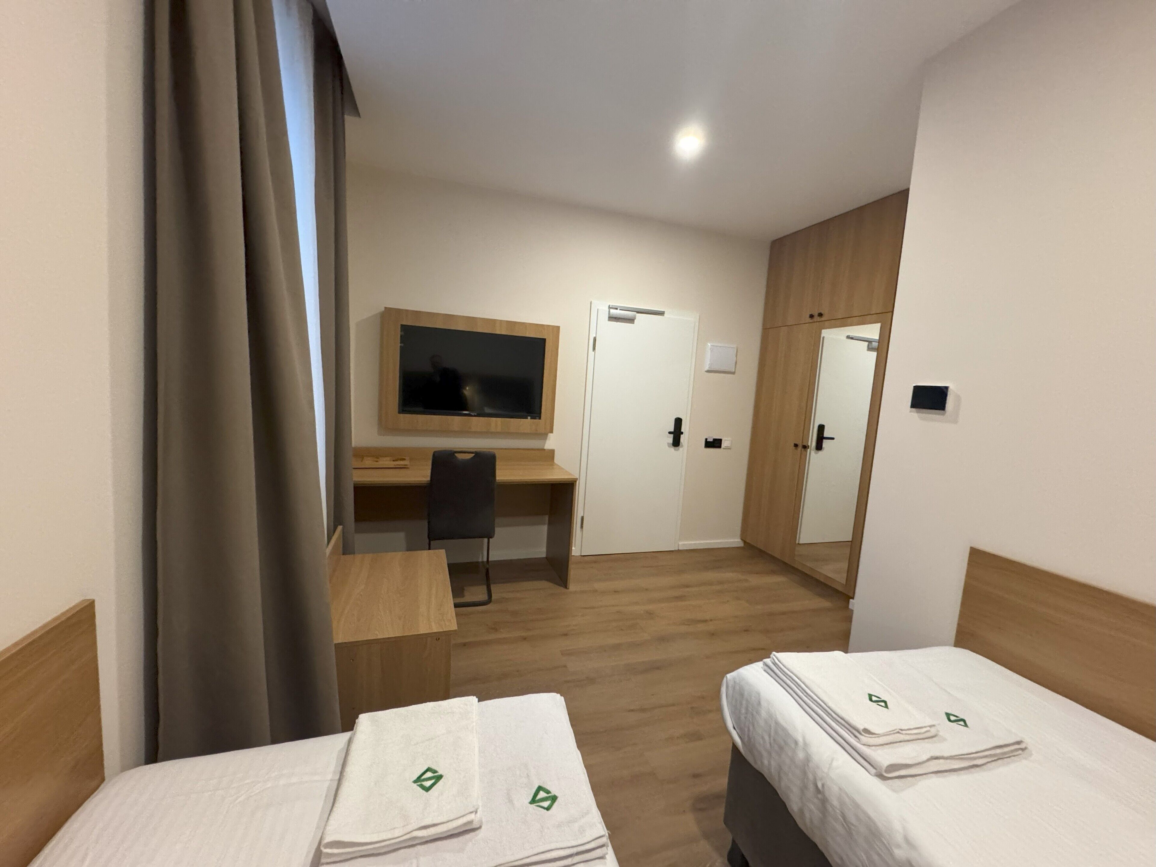 A hotel room with two beds, a desk, a chair, a TV, and a mirror.