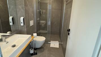 Un baño moderno con un espejo grande, lavamanos, inodoro y cabina de ducha.