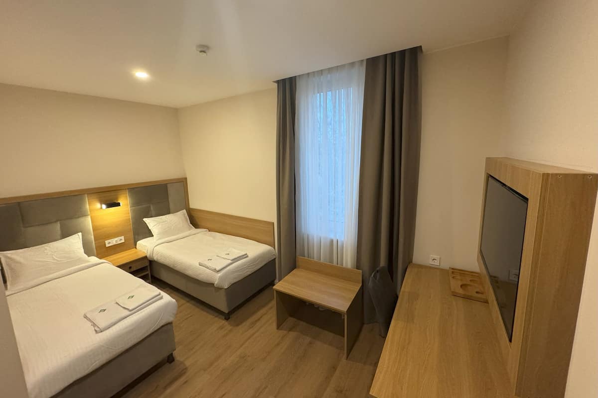 A hotel room with two beds, a desk, a TV, and a window with curtains.