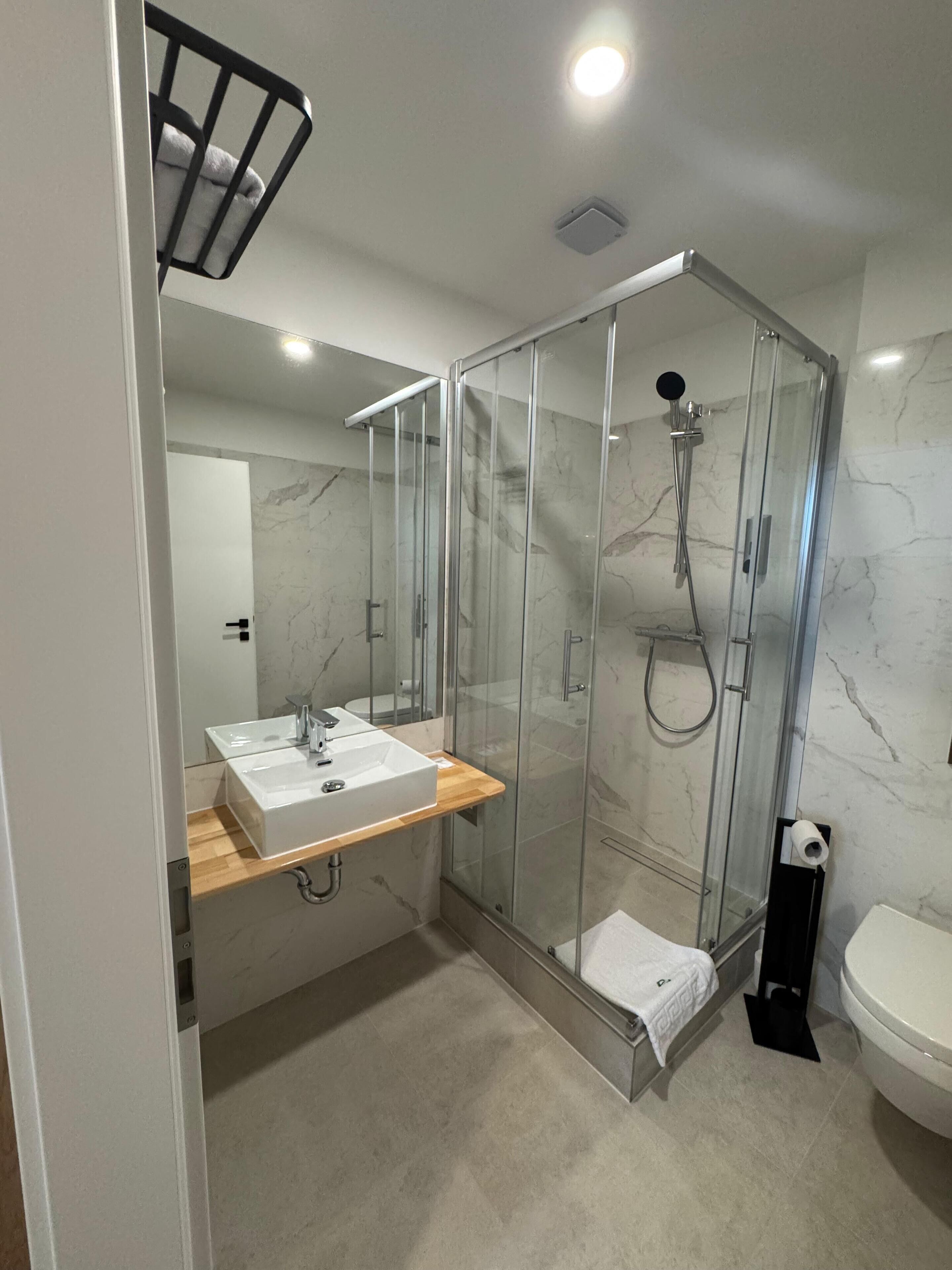 Un baño moderno con ducha envuelta en vidrio, un lavamanos blanco y encimera de madera, y un inodoro.