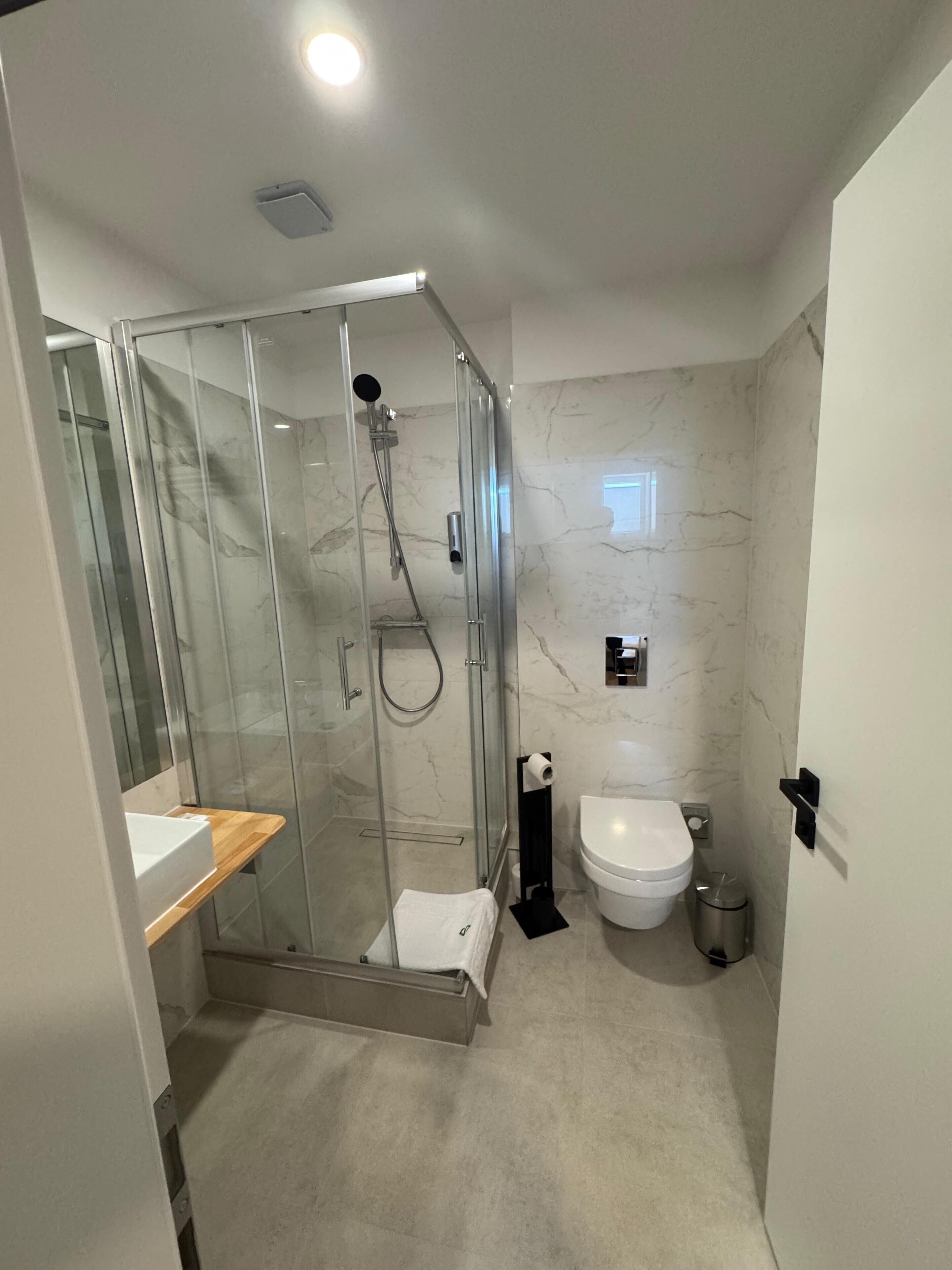 Ein modernes Badezimmer mit einer gläsernen Dusche, einer weißen Toilette und einer Wand mit Marmorfliesen.