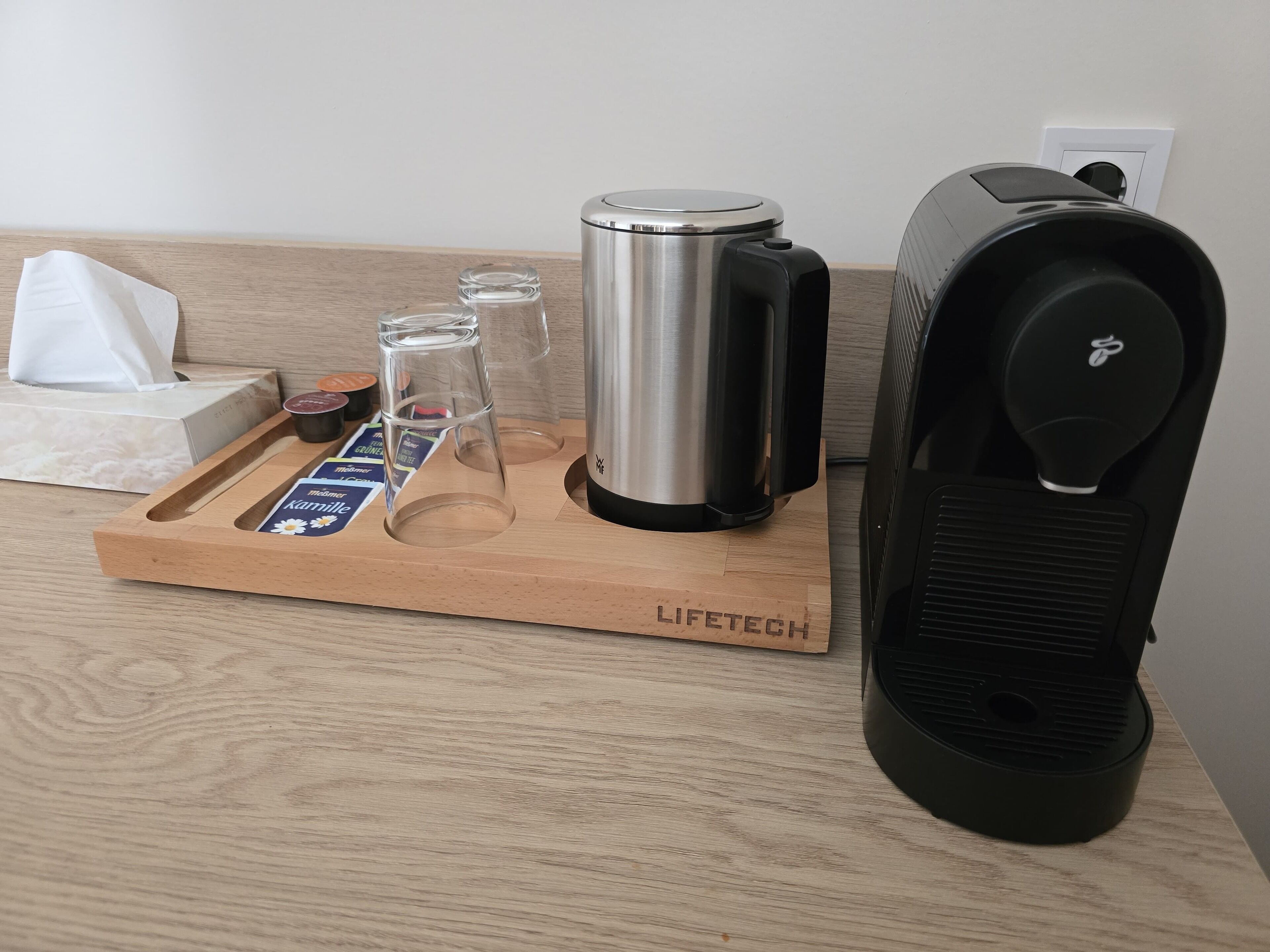 A wooden tray with a coffee maker, a water bottle, and a tissue box on a wooden surface.