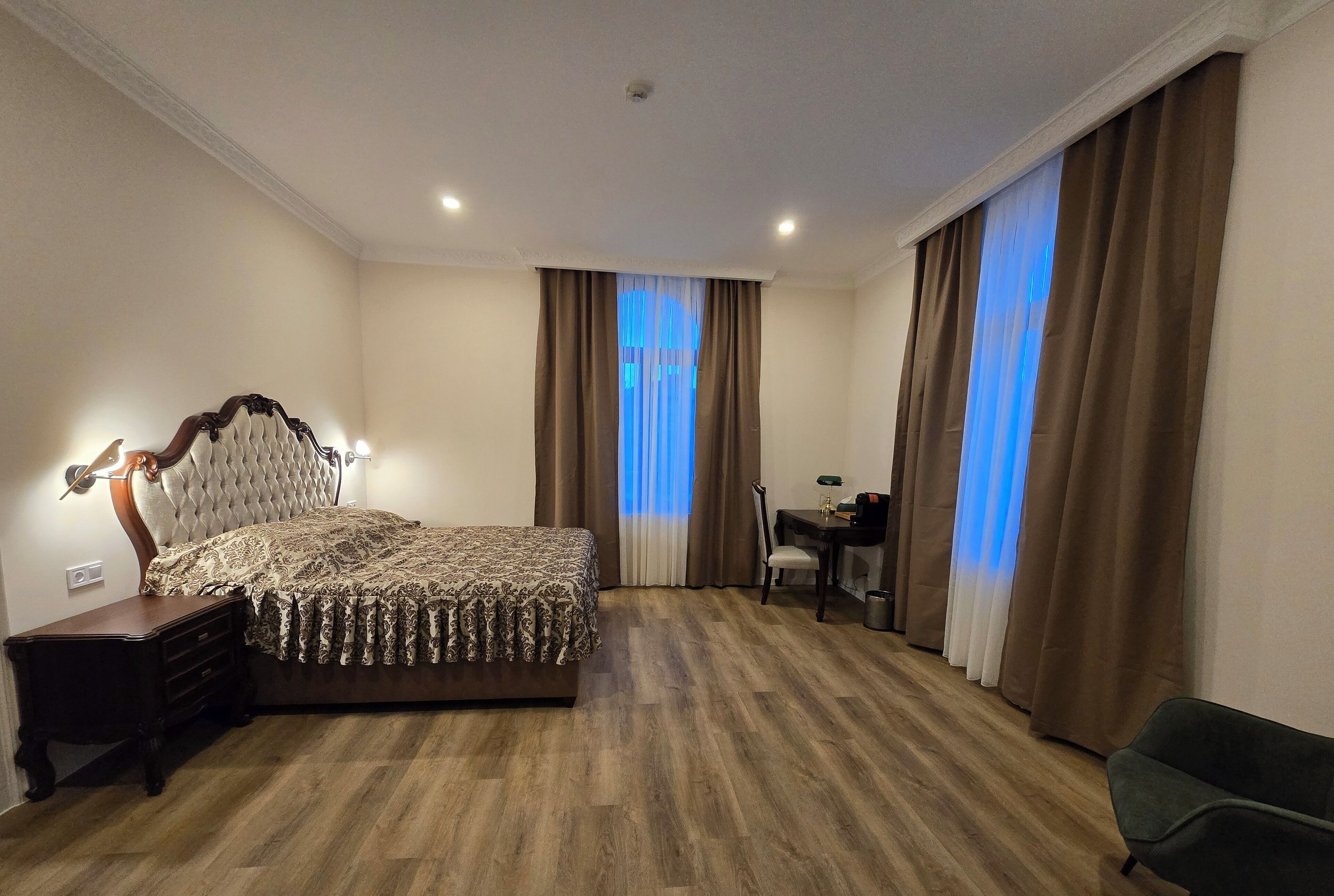 A hotel room with a large bed, a desk, a chair, and a small table.