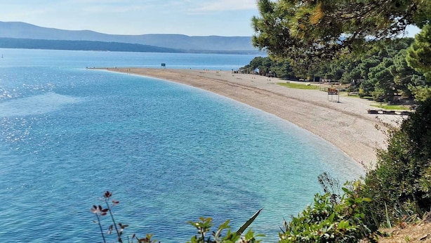 Une plage avec une eau d’un bleu limpide, un rivage sablonneux et quelques personnes.