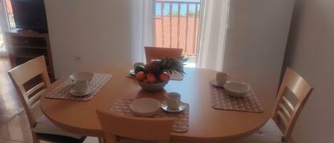 A dining table with a bowl of fruit, cups, and a clock on the wall.