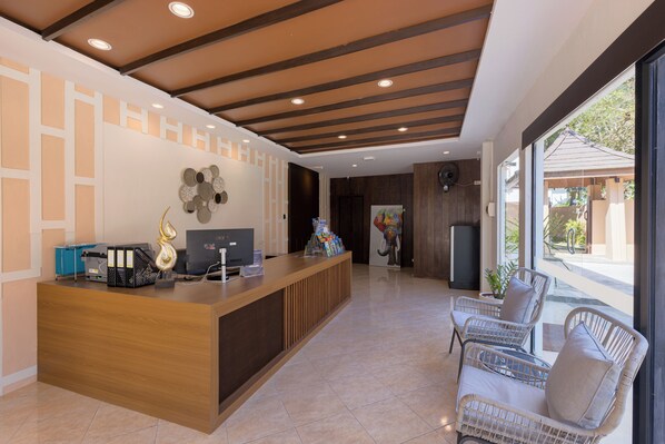 A reception area with a wooden desk, a television, and a seating area with wicker chairs. - Blue Palm Residence Kata (Karon)