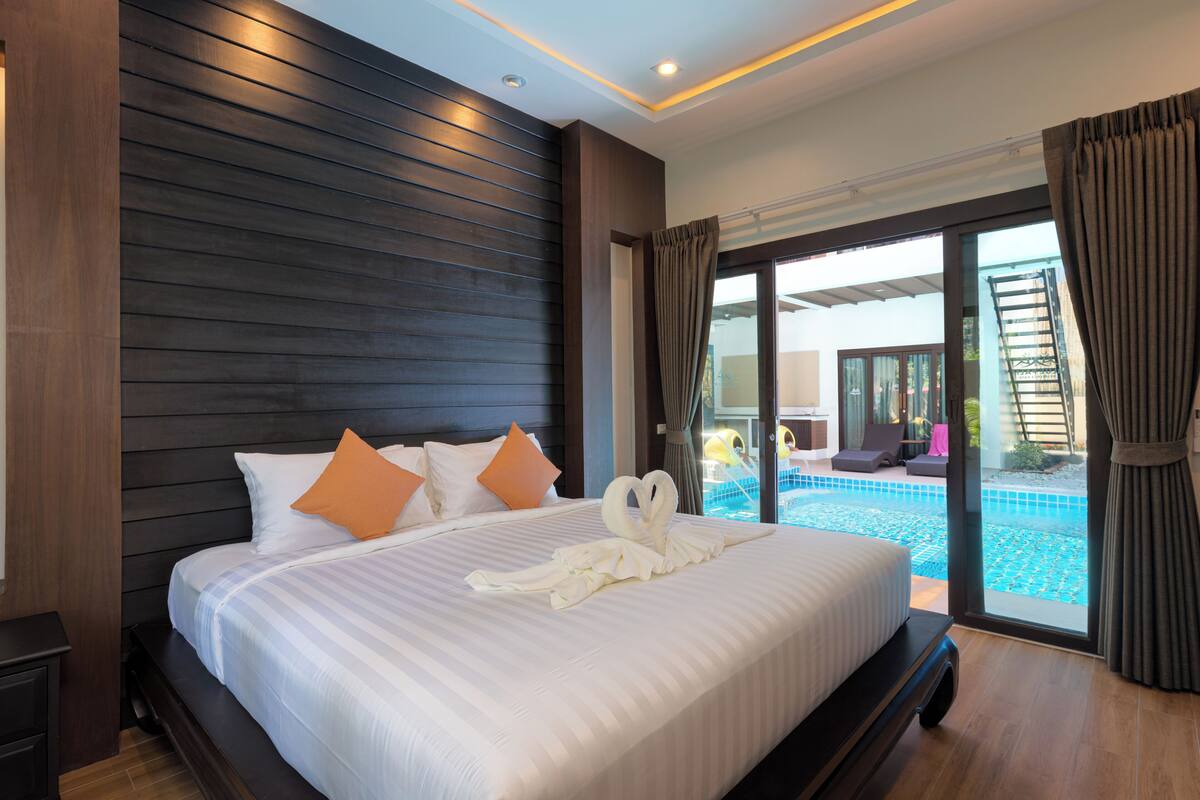 A large bed with a heart-shaped towel arrangement, a view of a swimming pool, and a balcony with a ladder.