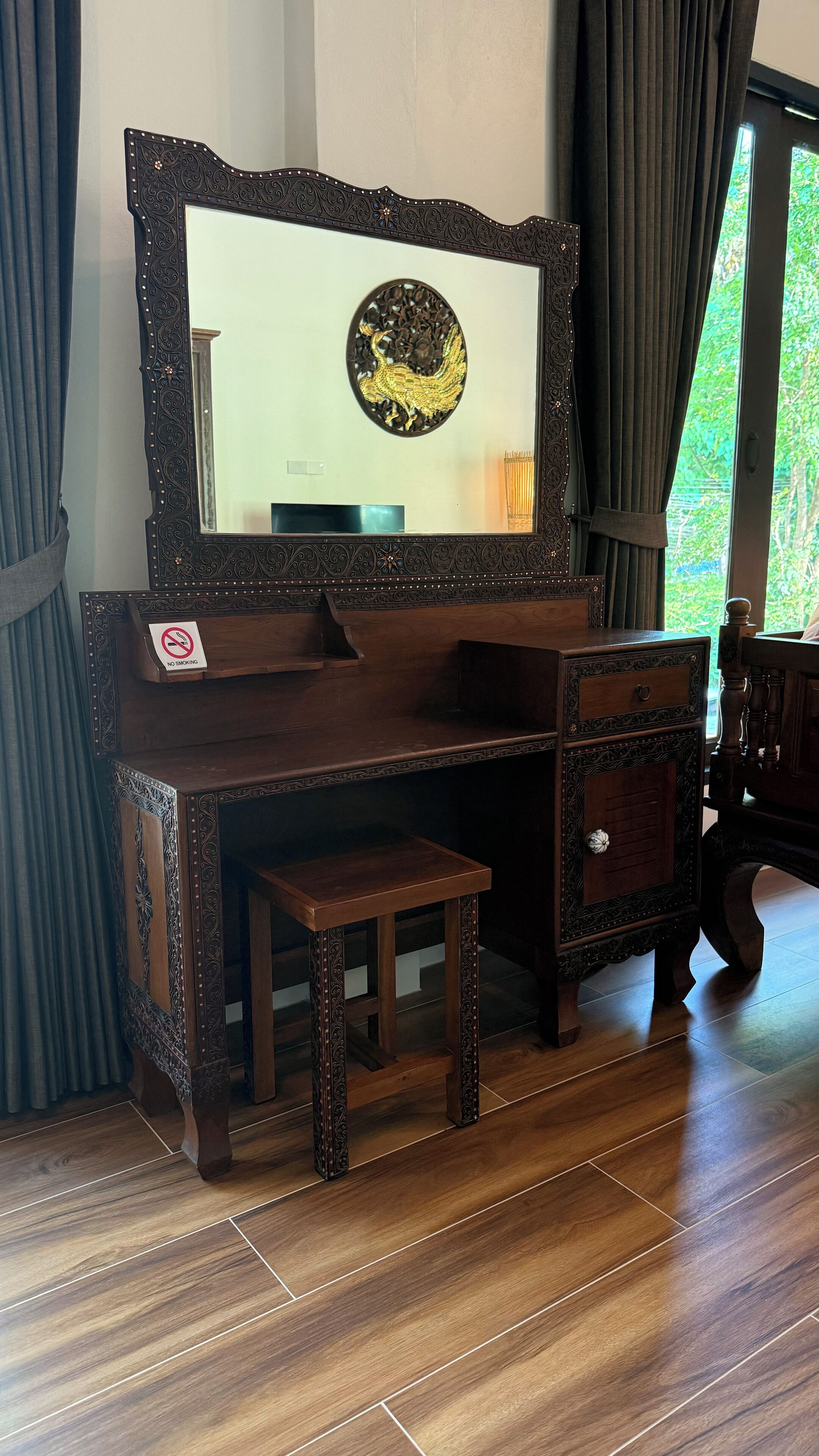 Un bureau en bois orné de sculptures complexes, un petit banc et un miroir décoratif orné d’un motif de coq.