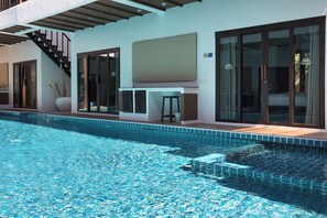 Un espace piscine moderne avec une piscine à l’eau cristalline, un bar et de grandes portes-fenêtres coulissantes donnant accès à une chambre.