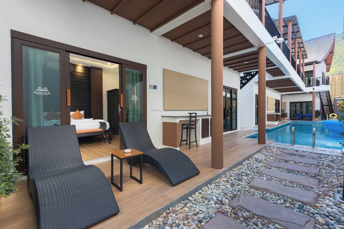 A hotel room with a bed, a sitting area with a chair and table, a pool, and a bar area.