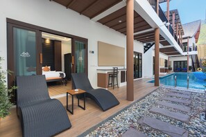 A hotel room with a bed, a sitting area with a chair and table, a pool, and a bar area. - Blue Palm Residence Kata (Karon)