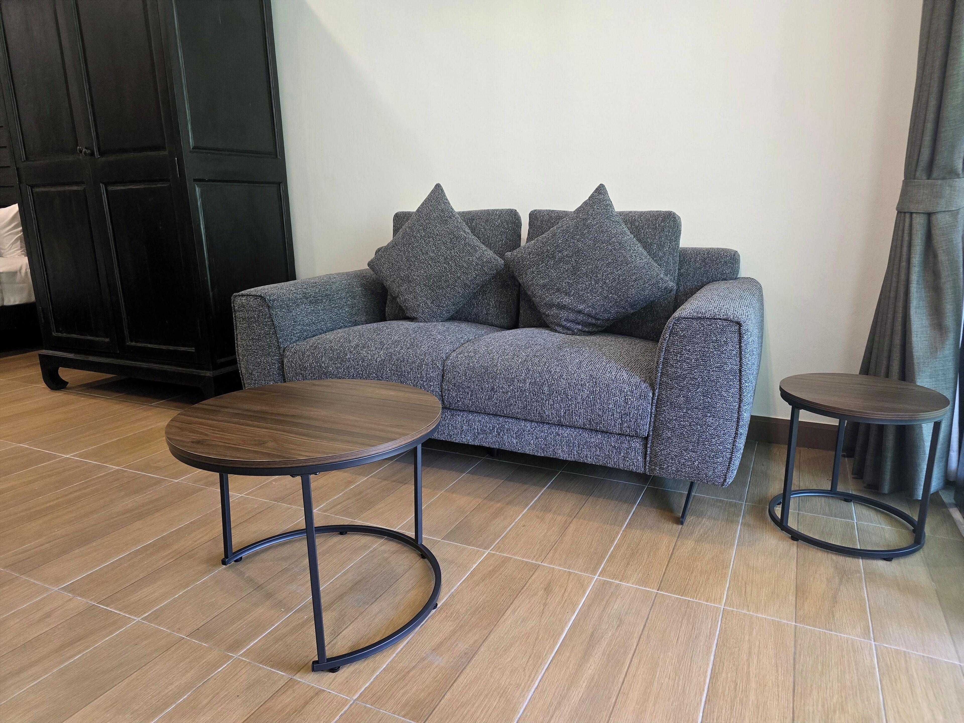 A modern living room with a grey sofa, two round tables, and a black cabinet.