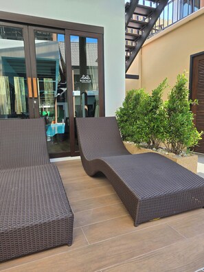 A modern outdoor seating area with wicker loungers and a small pool, adjacent to a building with a glass door and a staircase. - Blue Palm Residence Kata (Karon)