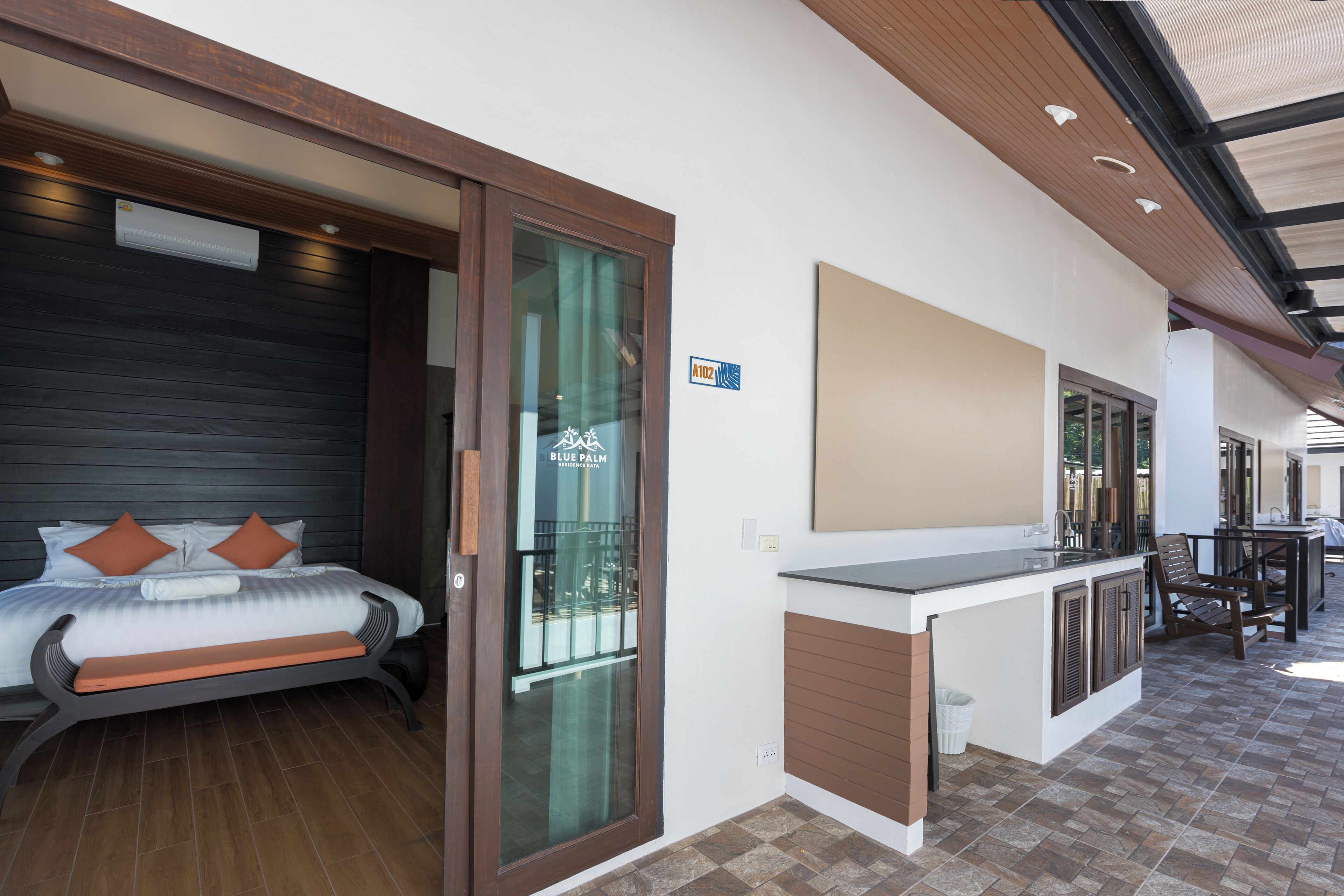 Quarto de hotel moderno com cama, um pequeno banco, porta de vidro que dá para uma varanda e área de kitchenette.