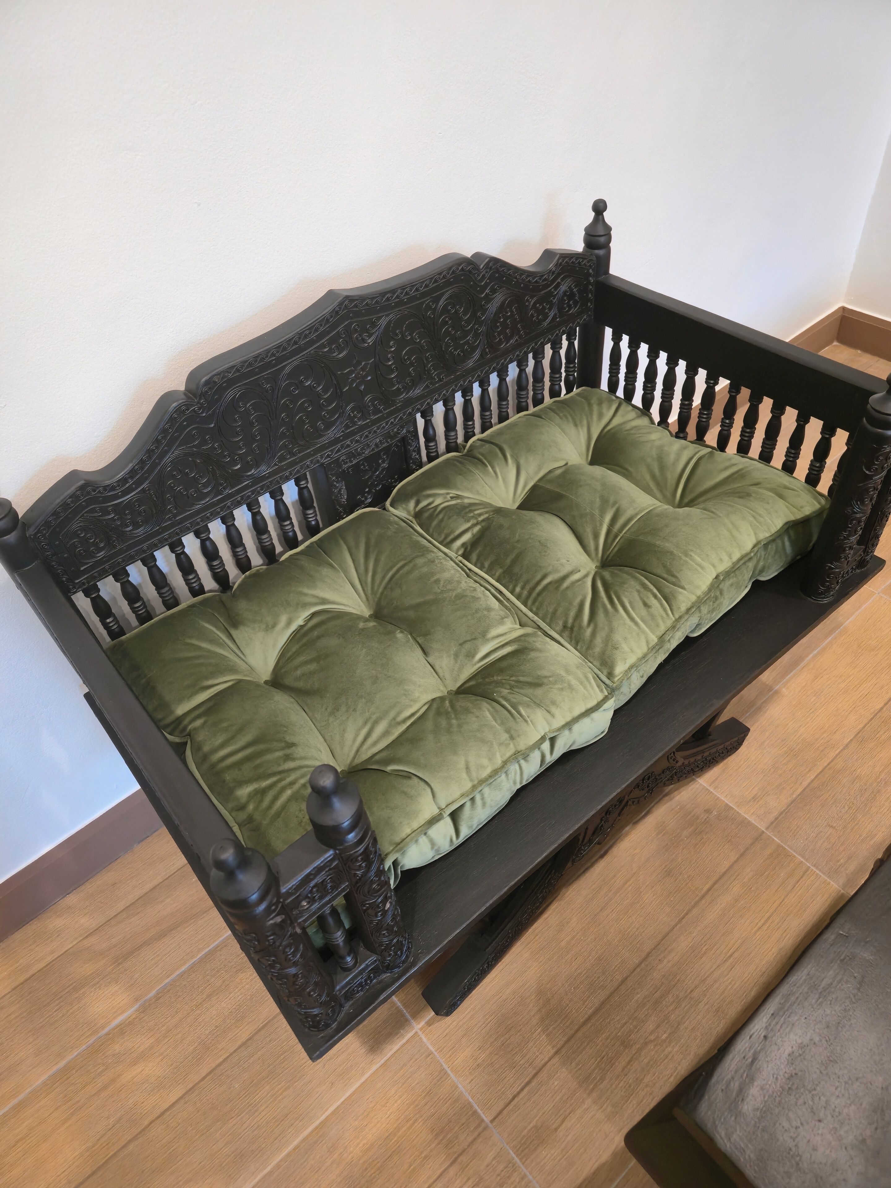 Un banco de madera oscura con tallas detalladas y un asiento acolchado verde.