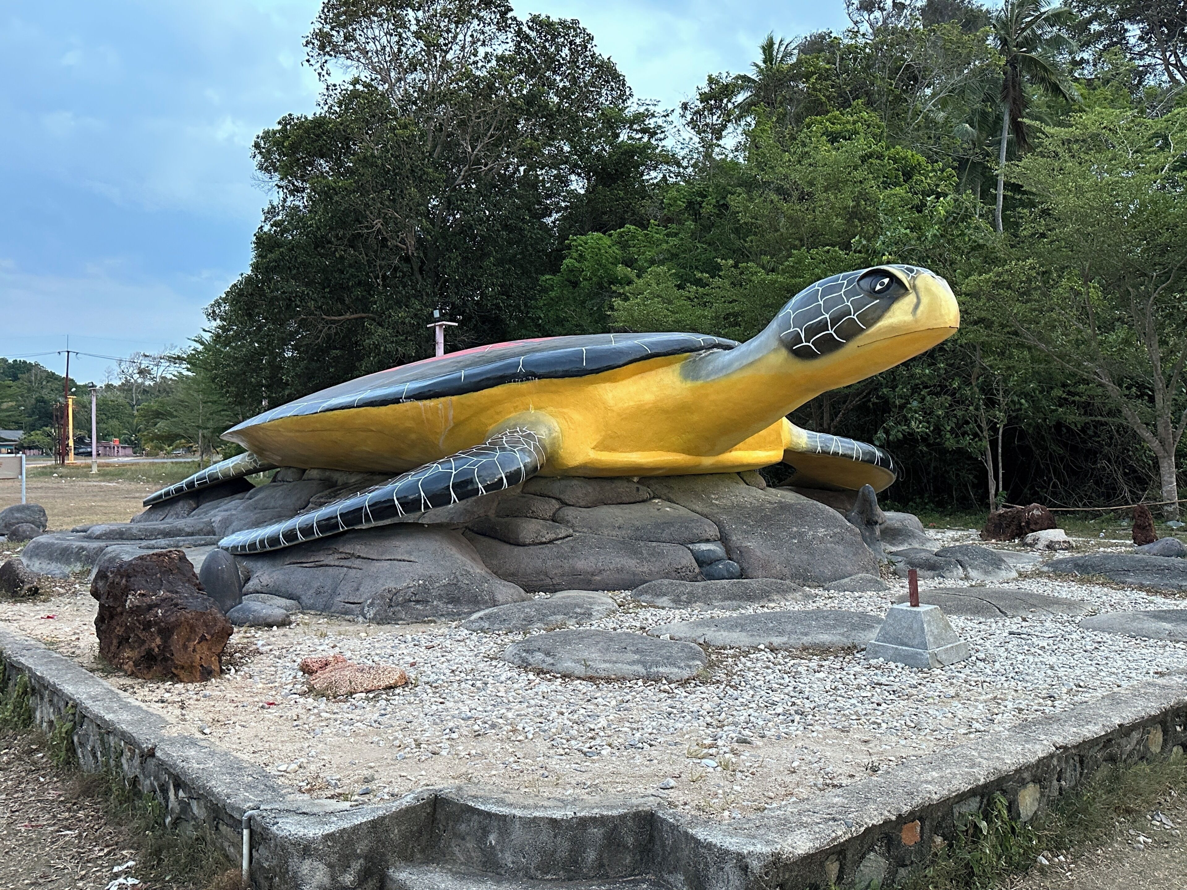 Una gran escultura de tortuga sobre una roca, con una zona pavimentada alrededor.