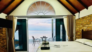 A bedroom with a bed, a table with chairs, and a view of the sea through an open door. - La Seahorse Homestay (Sebung)