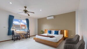 A modern hotel room with a large bed, a dining table with chairs, a ceiling fan, and a view of the outside. - Blue Palm Kata Resort (Karon)