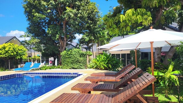 A swimming pool with wooden lounge chairs and a covered area. - Blue Palm Kata Resort (Karon)