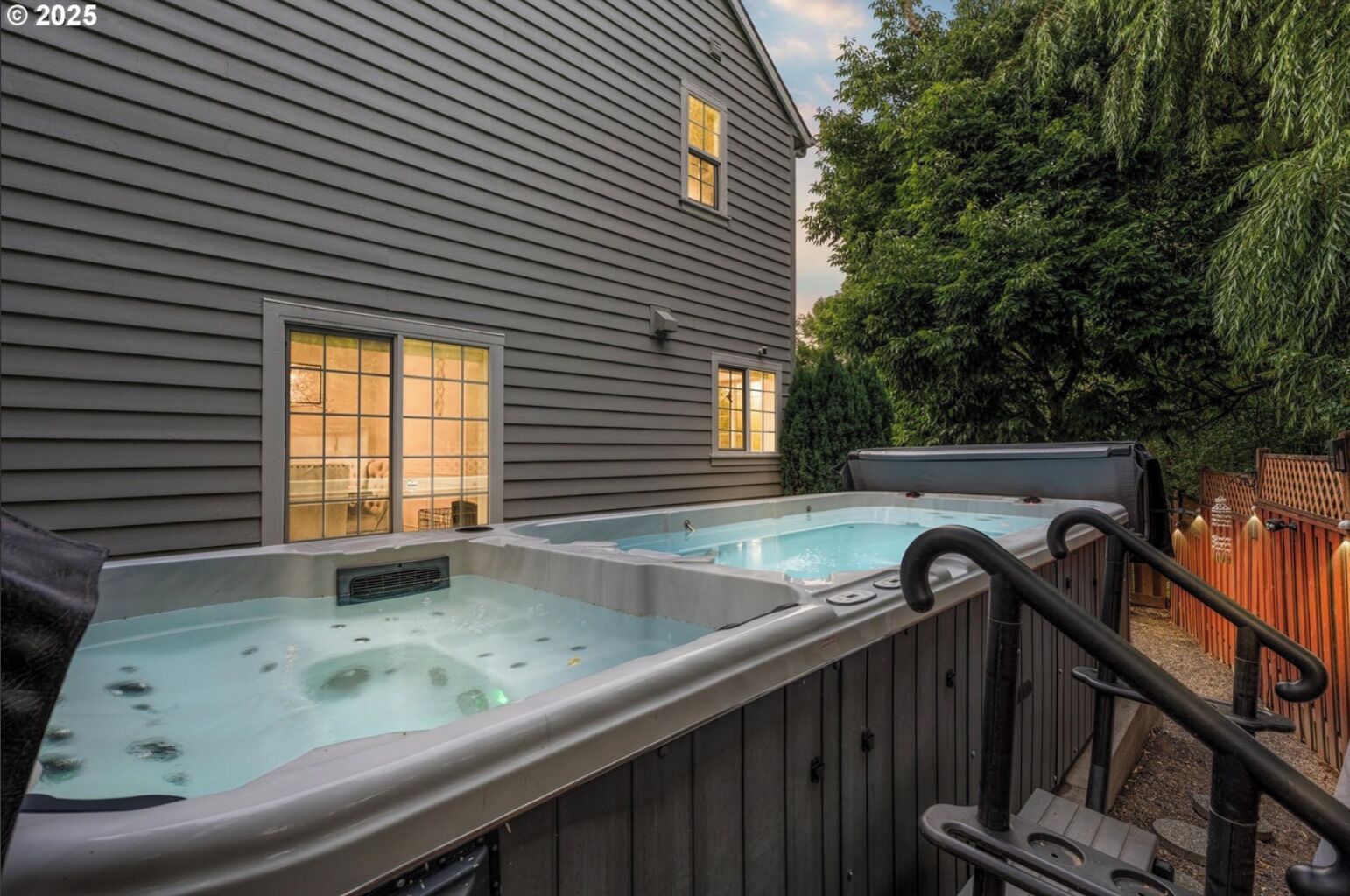 Un jardin avec deux bains à remous, une terrasse en bois et une maison dotée de baies vitrées latérales.