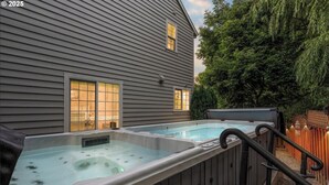 A backyard with two hot tubs, a wooden deck, and a house with sidelights. - Swim Spa + Hot Tub, Gazebo, BBQ Grill, 6 Bedrooms (Beaverton)