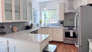 A modern kitchen with white cabinets, a marble countertop, a stainless steel refrigerator, and a built-in oven. - Swim Spa + Hot Tub, Gazebo, BBQ Grill, 6 Bedrooms (Beaverton)
