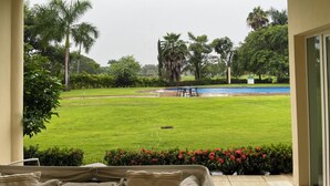 A covered outdoor area with a view of a well-maintained lawn, a pool, and surrounding greenery. - Poolside Condo, El Tigre. Beautiful (Nuevo Vallarta)